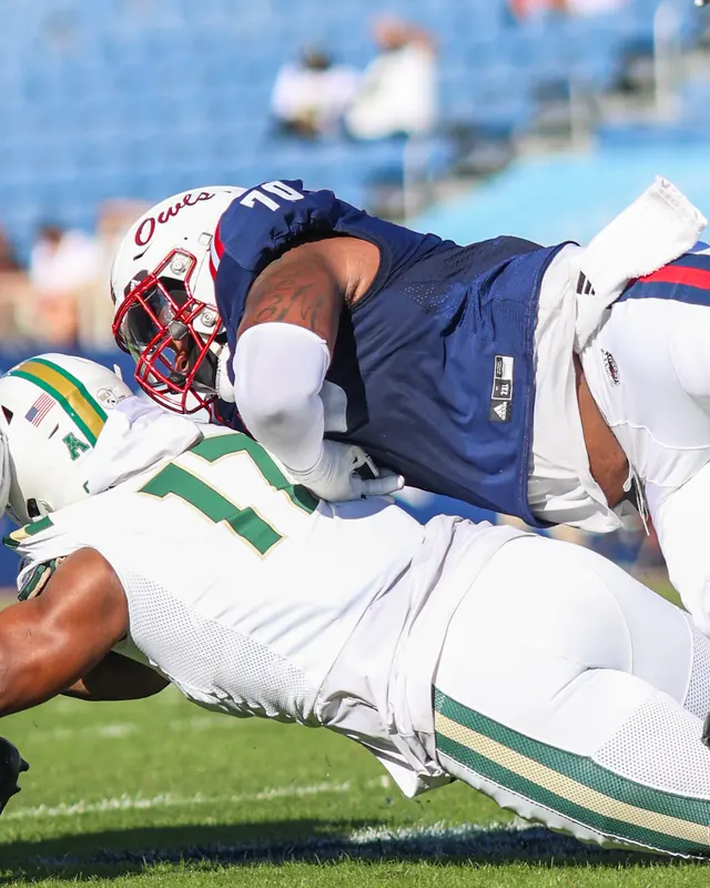 Malcolm in a navy Florida Atlantic jersey, number 70, driving a South Florida player to the ground
